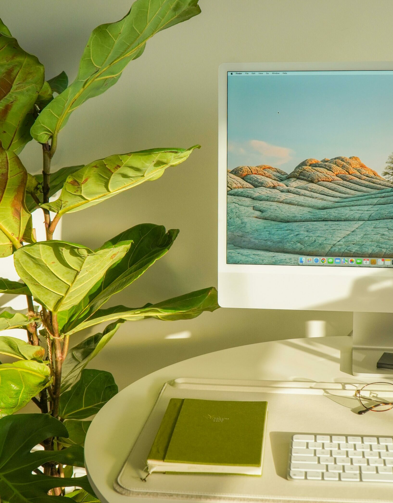 A bright and modern workspace featuring a computer, keyboard, notebook, and a lush green plant.
